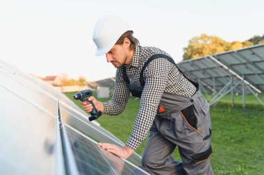 İşçi, güneşli bir günde metal kirişlere güneş paneli kuruyor. Yenilenebilir ve ekolojik enerji. Çevre fikri güvenli. Modern teknoloji ve yenilik. İş kıyafeti ve kask giyen bir adam..