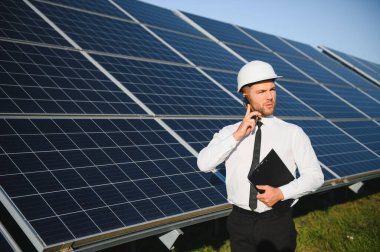 Kafkas mühendisi arka planda güneş paneli varken akıllı telefon kullanıyor. Alternatif elektrik kavramı.