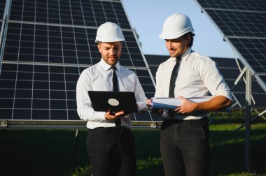 Güneş çiftliği, güneş paneli ve iki mühendis sistemin işleyişini kontrol etmek için yürür, dünyanın enerjisini korumak için alternatif enerji, temiz enerji üretimi için fotovoltaik modül fikri.