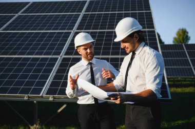 Güneş çiftliği, güneş paneli ve iki mühendis sistemin işleyişini kontrol etmek için yürür, dünyanın enerjisini korumak için alternatif enerji, temiz enerji üretimi için fotovoltaik modül fikri.