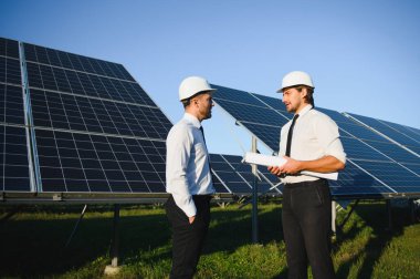 Güneş çiftliği, güneş paneli ve iki mühendis sistemin işleyişini kontrol etmek için yürür, dünyanın enerjisini korumak için alternatif enerji, temiz enerji üretimi için fotovoltaik modül fikri.