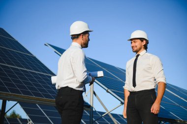 Güneş çiftliği, güneş paneli ve iki mühendis sistemin işleyişini kontrol etmek için yürür, dünyanın enerjisini korumak için alternatif enerji, temiz enerji üretimi için fotovoltaik modül fikri.