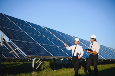 Güneş paneli çiftliği. İki Avrupalı mühendis güneş panellerini inceliyor. Güneş paneli çiftliğindeki işçiler.