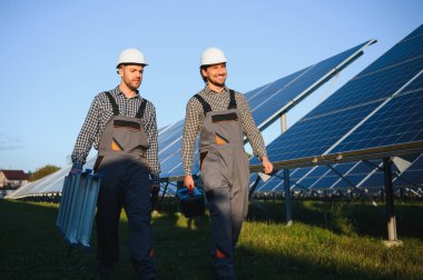 Gri üniforma giyen iki yetenekli işçi veya zanaatkar, teknisyenler temiz enerji ve elektrik tedariği için güneş panelleri kuruyorlar..