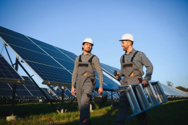 Gri üniforma giyen iki yetenekli işçi veya zanaatkar, teknisyenler temiz enerji ve elektrik tedariği için güneş panelleri kuruyorlar..