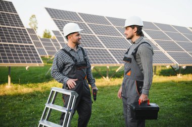 Gri üniforma giyen iki yetenekli işçi veya zanaatkar, teknisyenler temiz enerji ve elektrik tedariği için güneş panelleri kuruyorlar..