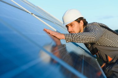 İşçi, güneşli bir günde metal kirişlere güneş paneli kuruyor. Yenilenebilir ve ekolojik enerji. Çevre fikri güvenli. Modern teknoloji ve yenilik. İş kıyafeti ve kask giyen bir adam..