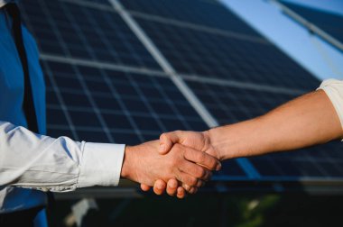 Güneş enerjisi istasyonundaki güneş panellerinin kurulumu ve bakımını denetlemek için çalıştıktan sonra iki Elektrik Mühendisi el sıkışıyor.