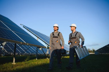 Gri üniforma giyen iki yetenekli işçi veya zanaatkar, teknisyenler temiz enerji ve elektrik tedariği için güneş panelleri kuruyorlar..