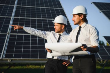 Güneş çiftliği, güneş paneli ve iki mühendis sistemin işleyişini kontrol etmek için yürür, dünyanın enerjisini korumak için alternatif enerji, temiz enerji üretimi için fotovoltaik modül fikri.