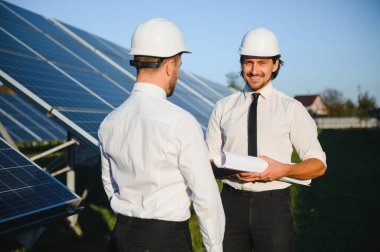 Güneş çiftliği, güneş paneli ve iki mühendis sistemin işleyişini kontrol etmek için yürür, dünyanın enerjisini korumak için alternatif enerji, temiz enerji üretimi için fotovoltaik modül fikri.