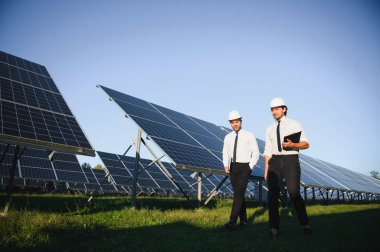 Yenilenebilir enerji. Bir güneş paneli çiftliğinin arka planında iki mühendis..