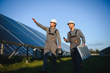 Gri üniforma giyen iki yetenekli işçi veya zanaatkar, teknisyenler temiz enerji ve elektrik tedariği için güneş panelleri kuruyorlar..