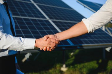 Güneş enerjisi istasyonundaki güneş panellerinin kurulumu ve bakımını denetlemek için çalıştıktan sonra iki Elektrik Mühendisi el sıkışıyor.