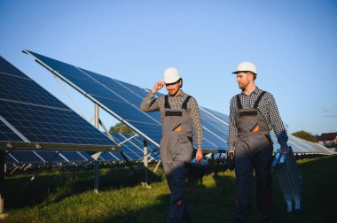Gri üniforma giyen iki yetenekli işçi veya zanaatkar, teknisyenler temiz enerji ve elektrik tedariği için güneş panelleri kuruyorlar..