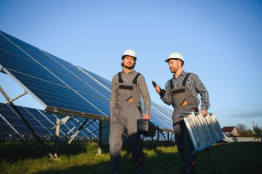 Gri üniforma giyen iki yetenekli işçi veya zanaatkar, teknisyenler temiz enerji ve elektrik tedariği için güneş panelleri kuruyorlar..