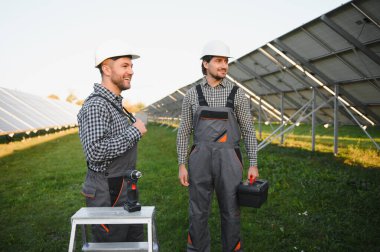 Gri üniforma giyen iki yetenekli işçi veya zanaatkar, teknisyenler temiz enerji ve elektrik tedariği için güneş panelleri kuruyorlar..