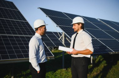 Yenilenebilir enerji. Bir güneş paneli çiftliğinin arka planında iki mühendis..