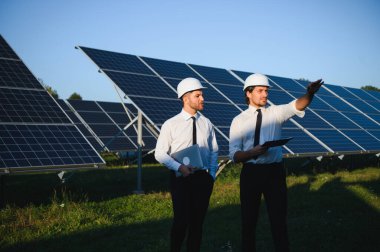 Yenilenebilir enerji. Bir güneş paneli çiftliğinin arka planında iki mühendis..