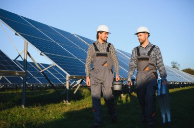 Gri üniforma giyen iki yetenekli işçi veya zanaatkar, teknisyenler temiz enerji ve elektrik tedariği için güneş panelleri kuruyorlar..