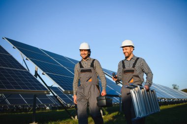 Gri üniforma giyen iki yetenekli işçi veya zanaatkar, teknisyenler temiz enerji ve elektrik tedariği için güneş panelleri kuruyorlar..