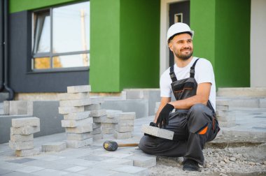 Eldivenlerin ustası katman katman taş döşüyordu. Profesyonel kaldırım işçisi tarafından kaldırım taşı döşenmiş. Kum temeli üzerine ev avlusunda gri beton döşeme döşeme döşeme döşeme.