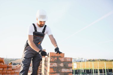 Construction worker man in work clothes and a construction helmet. Portrait of positive male builder in hardhat working at construction site.