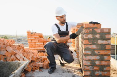 Construction worker man in work clothes and a construction helmet. Portrait of positive male builder in hardhat working at construction site.