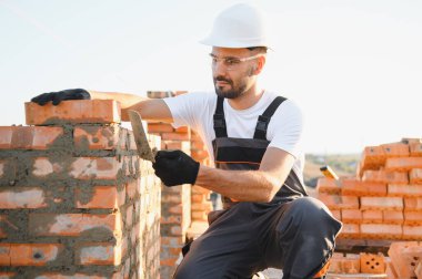 Construction worker man in work clothes and a construction helmet. Portrait of positive male builder in hardhat working at construction site.