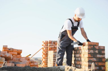 Construction worker man in work clothes and a construction helmet. Portrait of positive male builder in hardhat working at construction site.