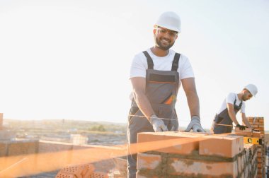 Önlüklü ve kasklı Hintli inşaat işçileri bir duvar örüyor..