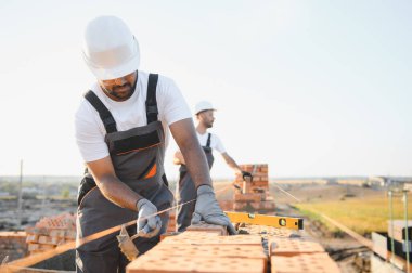 Önlüklü ve kasklı Hintli inşaat işçileri bir duvar örüyor..