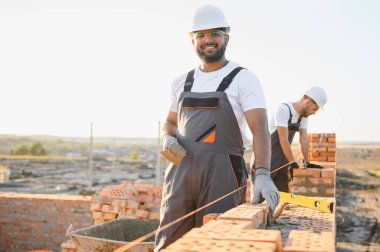 Önlüklü ve kasklı Hintli inşaat işçileri bir duvar örüyor..