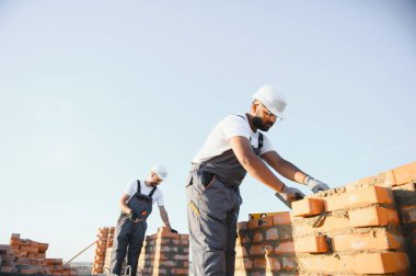 Hintli inşaat işçileri bir tuğla ev inşaatında çalışıyorlar. Bir tuğla duvar inşaatı.