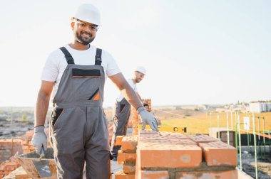 Hintli inşaat işçileri bir tuğla ev inşaatında çalışıyorlar. Bir tuğla duvar inşaatı.