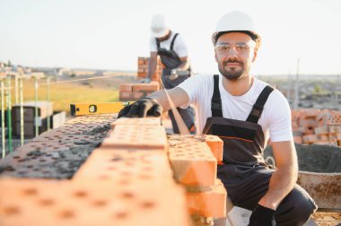 Construction worker man in work clothes and a construction helmet. Portrait of positive male builder in hardhat working at construction site.