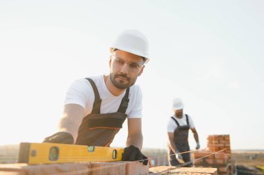İnşaatçılar inşaat alanında işçi tulumları ve kasklarıyla çalışıyorlar. Tuğla duvar inşaatı. Sanayi teması.