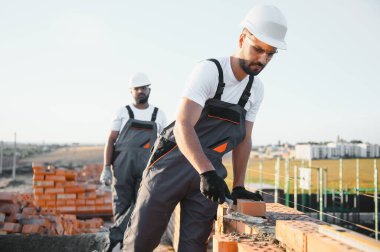 Construction worker man in work clothes and a construction helmet. Portrait of positive male builder in hardhat working at construction site.