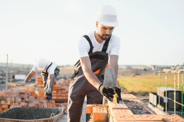 Construction worker man in work clothes and a construction helmet. Portrait of positive male builder in hardhat working at construction site.