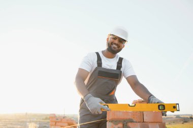 Construction worker man in work clothes and a construction helmet. Portrait of positive male builder in hardhat working at construction site.