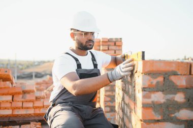 Tuğla duvar kuruluyor. Üniformalı inşaat işçisi ve güvenlik ekipmanı inşaatında çalışıyor.