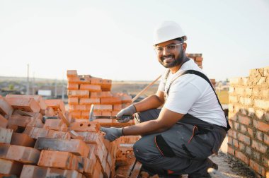 Construction worker man in work clothes and a construction helmet. Portrait of positive male builder in hardhat working at construction site.