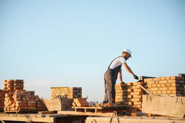 Tuğla duvar kuruluyor. Üniformalı inşaat işçisi ve güvenlik ekipmanı inşaatında çalışıyor.