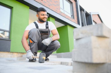 Hintli İşçi ustalıkla kaldırım taşı döşeyip çekiç kullanıyor ve eldiven takıyor..