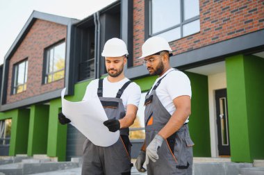 İnşaat planını yeni kulübelerin arka planıyla karşılaştıran iki mimar veya müteahhit..