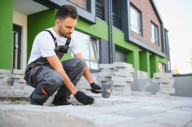 Eldivenlerin ustası katman katman taş döşüyordu. Profesyonel kaldırım işçisi tarafından kaldırım taşı döşenmiş. Kum temeli üzerine ev avlusunda gri beton döşeme döşeme döşeme döşeme.