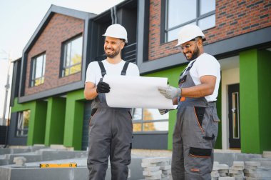 Two builders or architects checking the construction plan against the background of new cottages. clipart