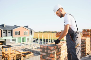 Construction worker man in work clothes and a construction helmet. Portrait of positive male builder in hardhat working at construction site.