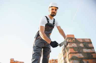 Construction worker man in work clothes and a construction helmet. Portrait of positive male builder in hardhat working at construction site.