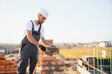 Construction worker man in work clothes and a construction helmet. Portrait of positive male builder in hardhat working at construction site.